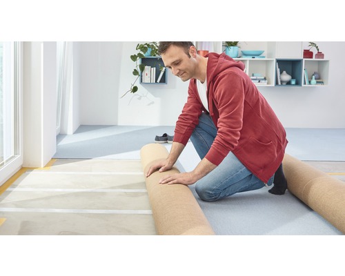 Mann verlegt Teppichboden in einem hellen Raum.