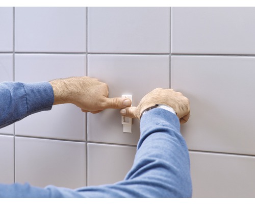 Eine Person befestigt einen Fliesenjustierer an einer gefliesten Wand.