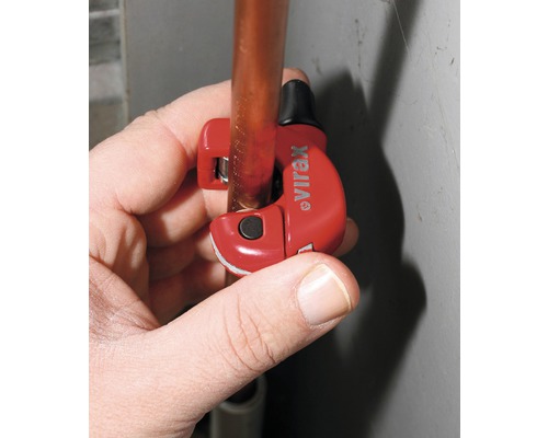 Eine Hand schneidet ein Kupferrohr mit einem Rohrabschneider der Marke Virax.