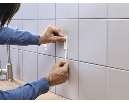 Person befestigt eine Fliesen Nivellierhilfe an einer gefliesten Wand