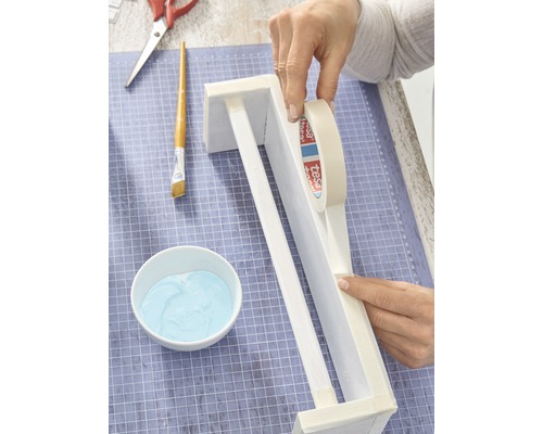 Bastelszene mit Händen, Malerkrepp, Pinsel, Farbe und Schere auf einer Schneidematte