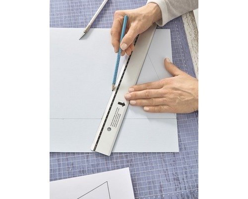 Person, die mit einem Bleistift und einem Lineal auf einem Schneidebrett eine Linie auf ein Stück Papier zeichnet