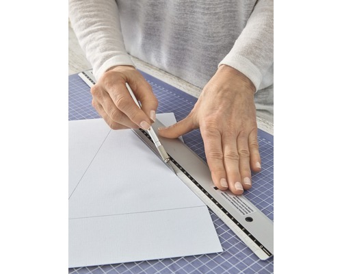 Person schneidet Papier mit Cutter und Lineal auf einer Schneidematte