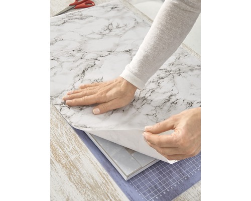 Person bringt selbstklebende Folie in Marmoroptik an