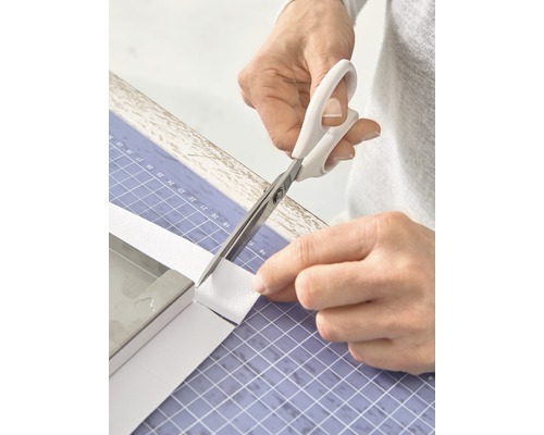 Person schneidet mit einer Schere ein weißes Band auf einer Schneidematte zu