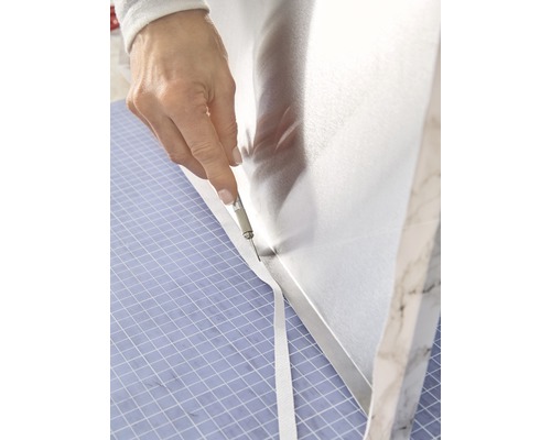 Eine Person schneidet mit einem Cuttermesser eine Schutzfolie auf einer Arbeitsfläche zu.