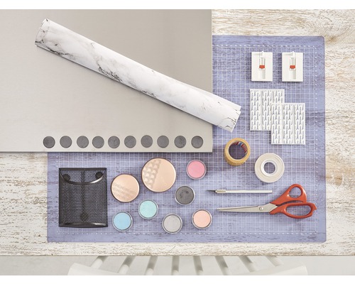 Bastelutensilien auf einem Tisch, darunter Folie, Schneidematte, Kleber, Schere und Farben