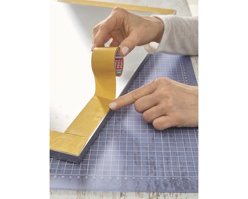 Person klebt doppelseitiges Klebeband auf einen Spiegelrahmen