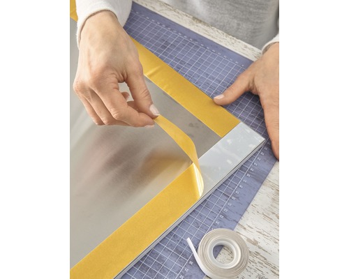 Person befestigt Spiegel mit doppelseitigem Klebeband auf einer Schneidematte.