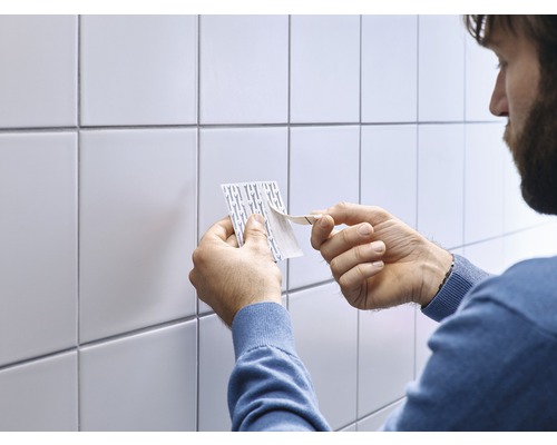 Person entfernt Schutzfolie von Klebestreifen vor weißen Fliesen