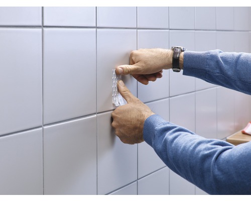 Doppelseitiges Klebeband wird an einer Wandfliese befestigt.