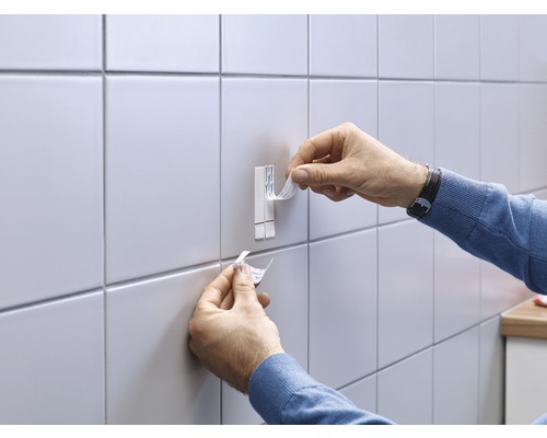 Person befestigt einen Klebehaken an einer gefliesten Wand.