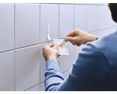 Mann befestigt Klebestreifen an der Fliesenwand