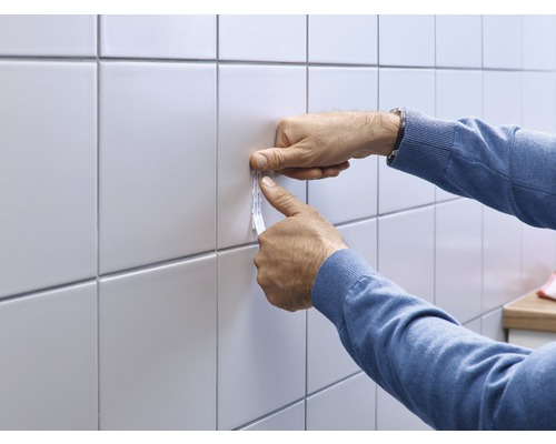 Anwendung von Klebestreifen auf Fliesen durch eine Person