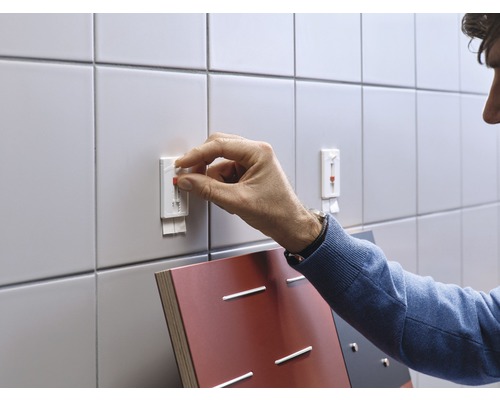 Person befestigt einen Klebehaken an einer gefliesten Wand