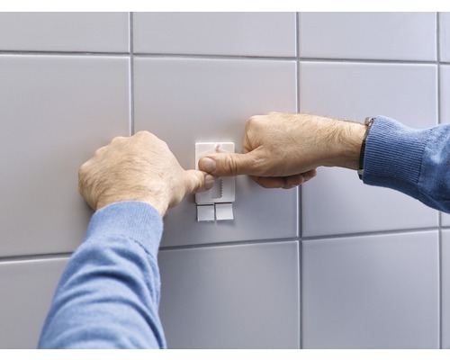 Person befestigt einen Klebehaken an einer gefliesten Wand.