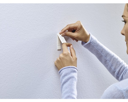 Frau befestigt einen Klebehaken an der Wand