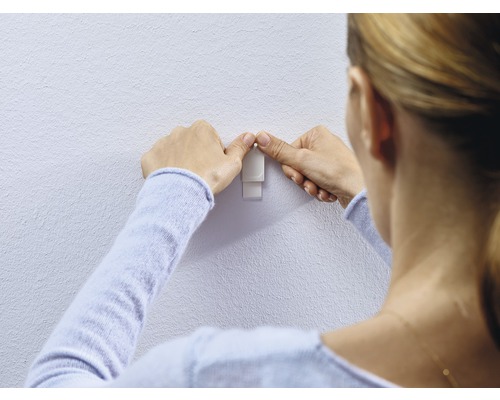 Frau befestigt einen Klebehaken an der Wand
