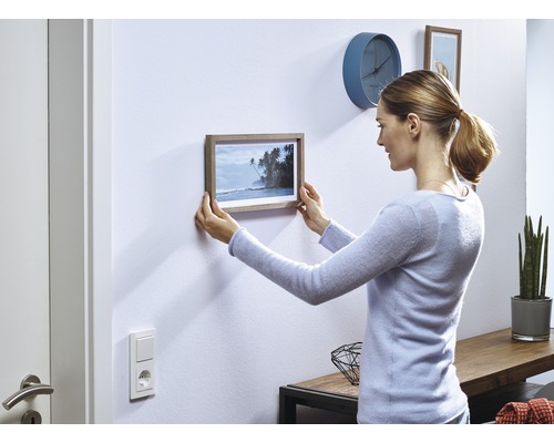 Frau hängt ein Bild mit Holzrahmen an die Wand