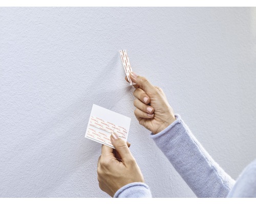 Eine Person befestigt Klebestreifen an einer Wand