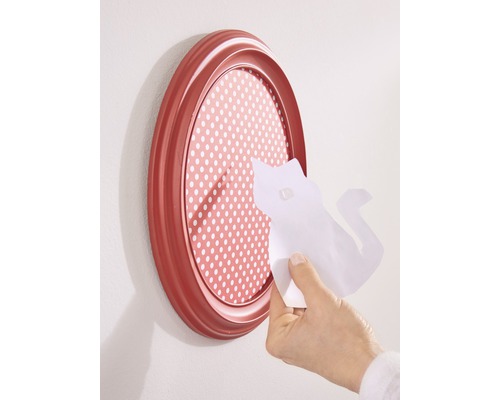 Ovaler Bilderrahmen mit gepunktetem Hintergrund und einer Hand, die ein Papierstück mit einer Katzenform anbringt