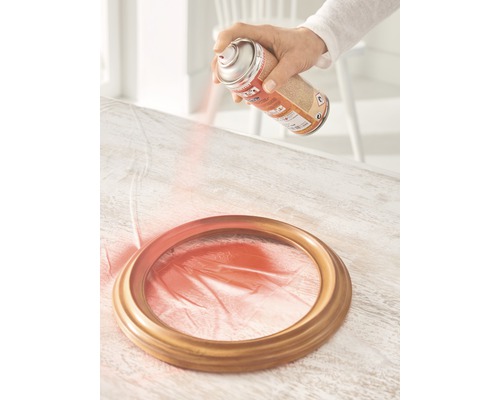 Eine Person sprüht Farbe auf einen Bilderrahmen mit einer Sprühdose.