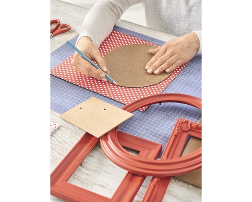 Basteltisch mit Händen, die einen Kreis auf ein Blatt Papier zeichnen, umgeben von Bastelmaterialien und Bilderrahmen