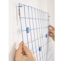 Person befestigt eine blaue Gittertafel mit Magneten an der Wand.