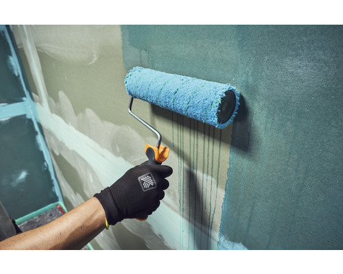Hand mit Arbeitshandschuh streicht eine Wand mit einer Farbwalze