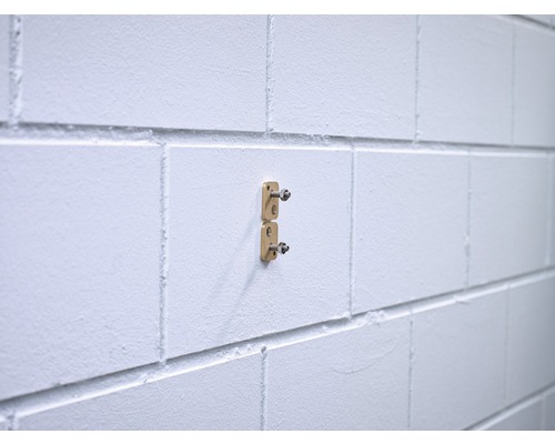 Zwei goldfarbene Halterungen sind an einer weißen Wand befestigt.