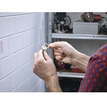 Eine Person befestigt einen selbstklebenden magnetischen Verschluss an einer Wand.