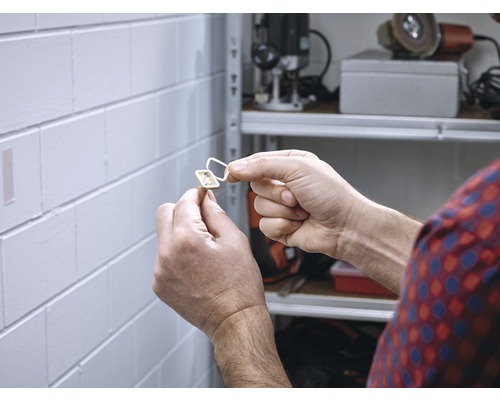 Eine Person befestigt einen selbstklebenden magnetischen Verschluss an einer Wand.