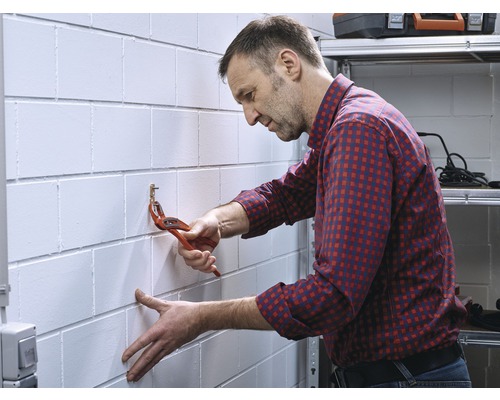 Mann befestigt einen Haken mit einer Rohrzange an einer Wand.