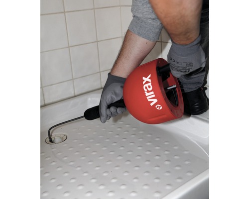 Eine Person benutzt eine Rohrreinigungsspirale der Marke Virax in einer Duschwanne, um eine Verstopfung zu lösen.