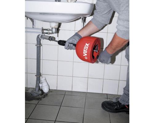Eine Person benutzt eine Rohrreinigungsspirale unter einem Waschbecken, um eine Verstopfung zu beseitigen.