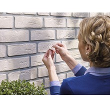 Frau befestigt Befestigungselement an einer Wand mit Backsteinoptik