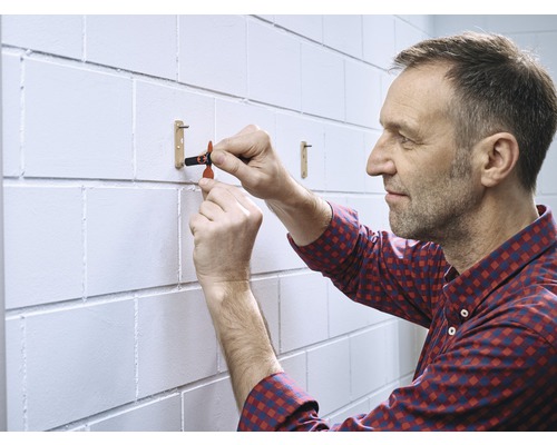 Ein Mann befestigt eine Kleiderstange an einer weißen Ziegelwand.