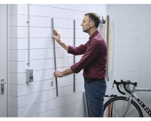 Mann montiert eine Metallschiene an einer Wand zur Aufbewahrung von Gegenständen in einer Garage oder einem Keller.