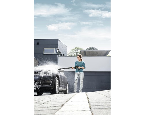 Frau reinigt Auto mit Hochdruckreiniger vor Haus