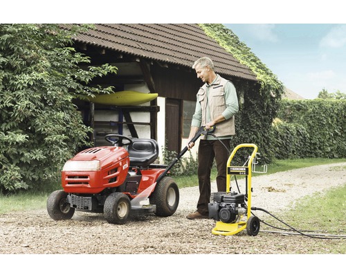Ein Mann bedient einen Kärcher Hochdruckreiniger neben einem Rasentraktor im Garten.