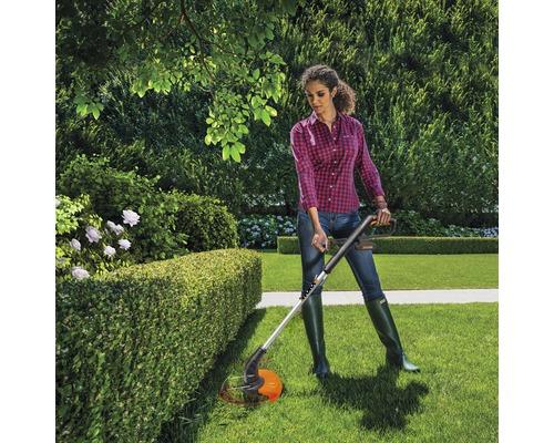 Frau schneidet Hecke mit einem Rasentrimmer im Garten.