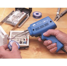 Eine Person benutzt eine Lötpistole zum Löten von elektronischen Bauteilen in einem Gehäuse. Lötzinn, Multitool und weitere elektronische Bauteile liegen auf einem Tisch.