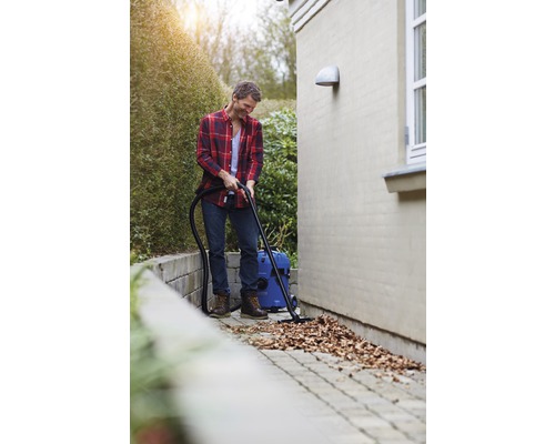 Ein Mann säubert mit einem Nass Trockensauger Laub von einem Pflasterweg.
