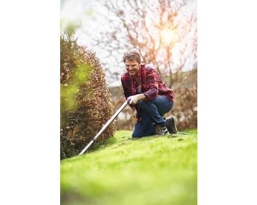 Ein Mann kniet im Garten und schneidet mit einem Kantenschneider Rasenkanten.