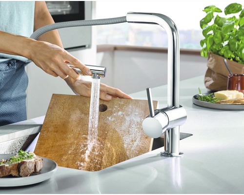 Küchenszene mit Armatur, Wasserstrahl und Person, die ein Schneidebrett reinigt
