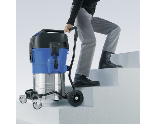 Eine Person zieht einen Industriestaubsauger mit Trolley über eine Treppe.