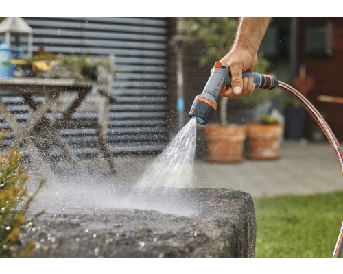 Person bewässert Stein mit einer Gartendusche und einem Gartenschlauch.