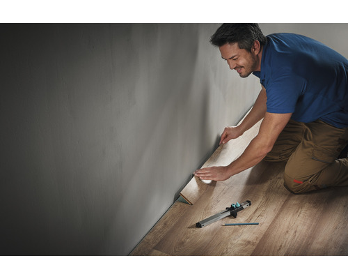 Mann verlegt Laminat mit Werkzeug entlang einer Wand