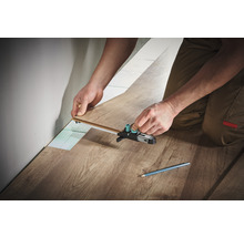 Person verlegt Laminat mit einem Anreißwerkzeug.