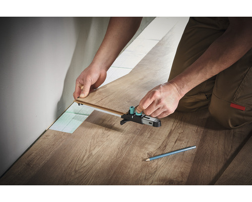 Person verlegt Laminat mit einem Anreißwerkzeug.